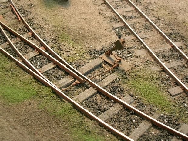 Eine Modell–Feldbahnweiche, daneben noch ein Gleis, im überwachsenen Gelände.