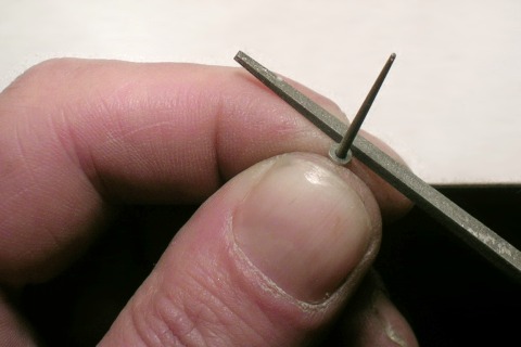 Großaufnahme: eine Rundfeile zwischen Daumen und Zeigefinger, darauf ein winziges Metallscheibchen, das mit der Feile entgratet wird.