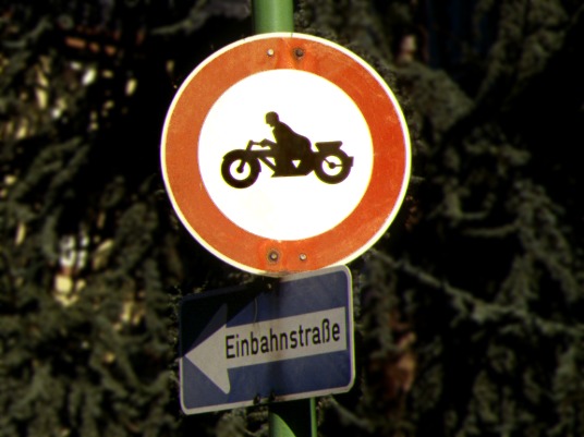 Rundes Verkehrsschild: schwarzer Motorradfahrer auf weißem Grund, mit rotem Außenring am Schild.