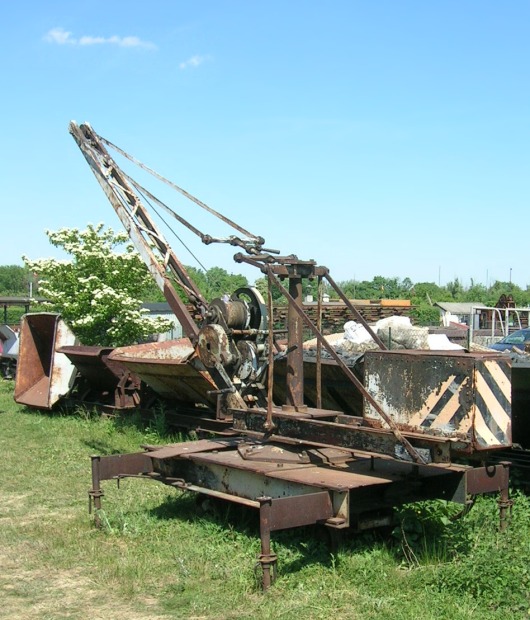 Rostiger Kranwagen vor Kipploren und blauem Himmel.