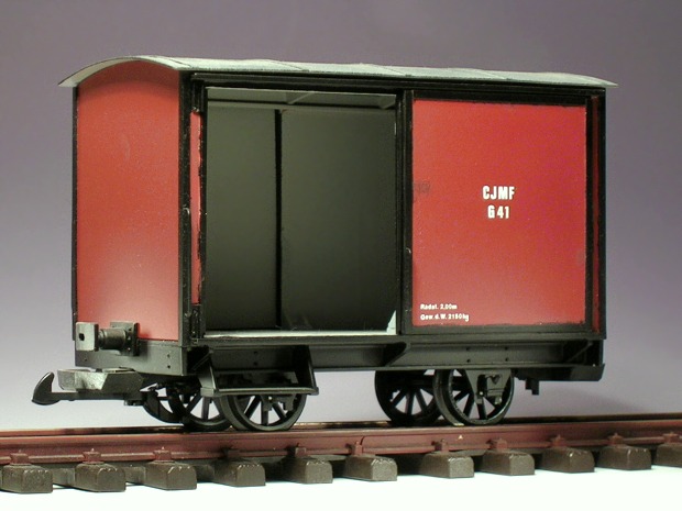 Modellfoto: kleiner, rotbrauner, geschlossener Güterwagen mit einer offenen Schiebetür, innen grau lackiert.