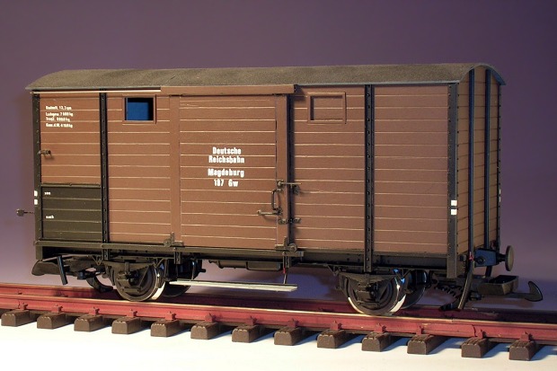 Modellfoto: Gedeckter Güterwagen mit braun lackiertem Bretteraufbau von der Seite gesehen.